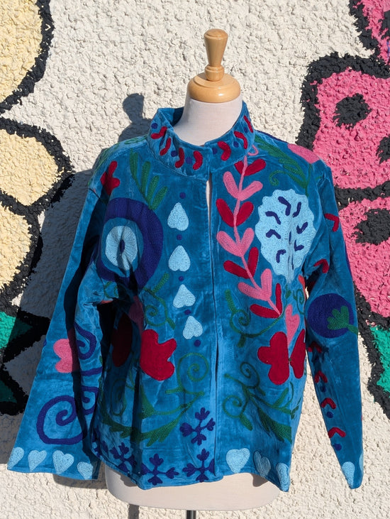 Colorful jacket with floral patterns on a mannequin against a textured wall.