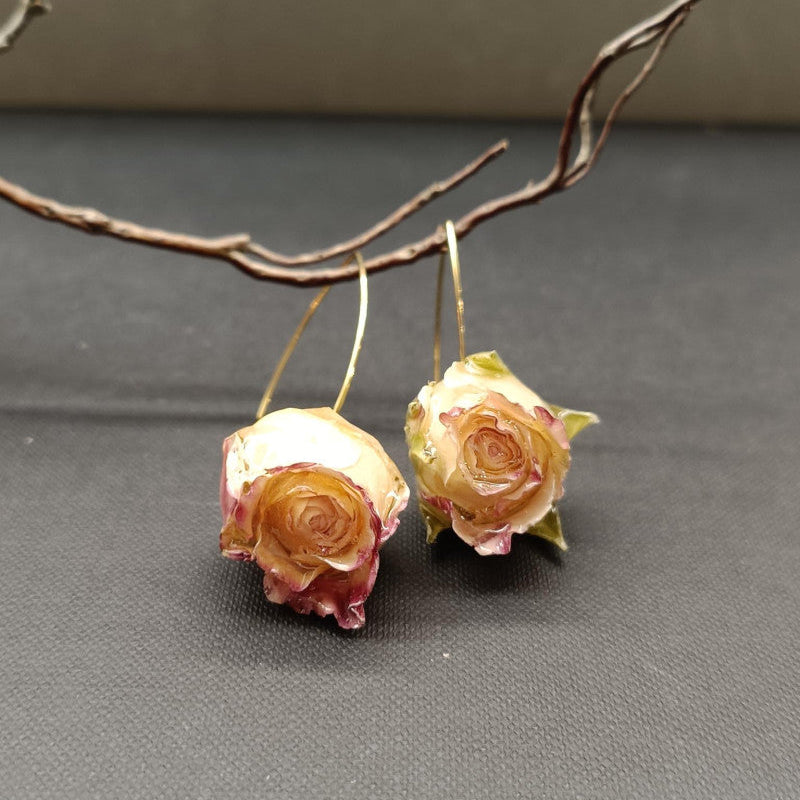 Pair of rose-shaped earrings on a gray surface with a branch in the background
