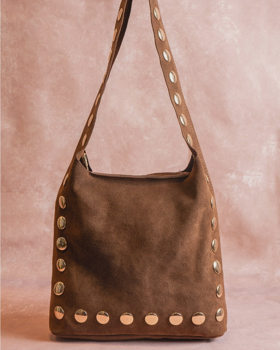 Brown suede handbag with studded details on a pink background