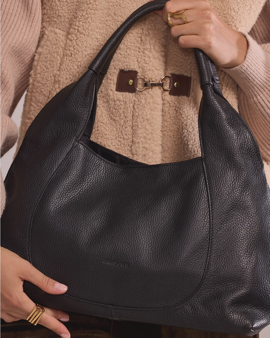Black leather handbag held by a person wearing a beige sweater.